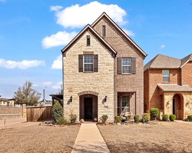 view of front facade featuring brick siding, fence, and stone siding
