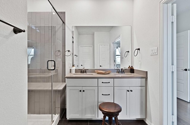 bathroom featuring a shower stall, a textured wall, double vanity, and a sink
