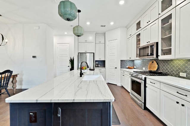 kitchen featuring white cabinets, stainless steel appliances, wood finished floors, decorative backsplash, and a kitchen island with sink