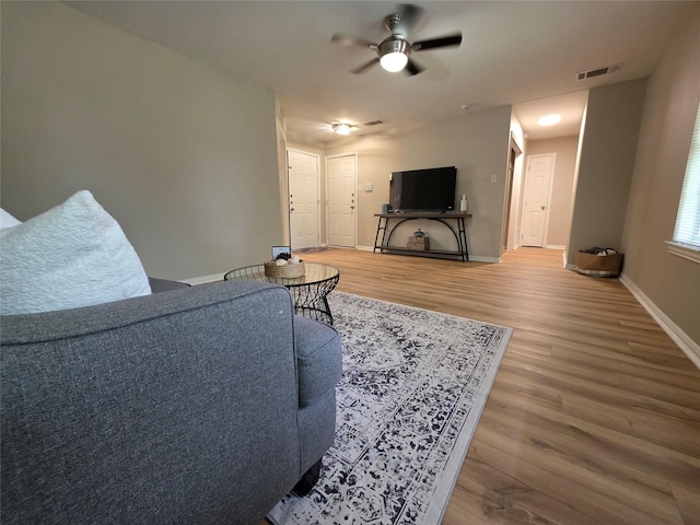 living room with baseboards, visible vents, wood finished floors, and a ceiling fan