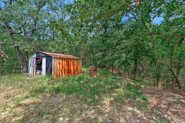 view of yard with a wooded view, an outbuilding, and a shed