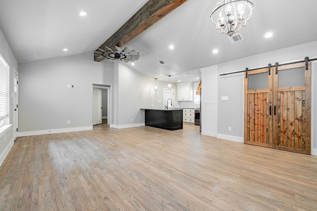 unfurnished living room featuring lofted ceiling with beams, light wood finished floors, a sink, a barn door, and visible vents