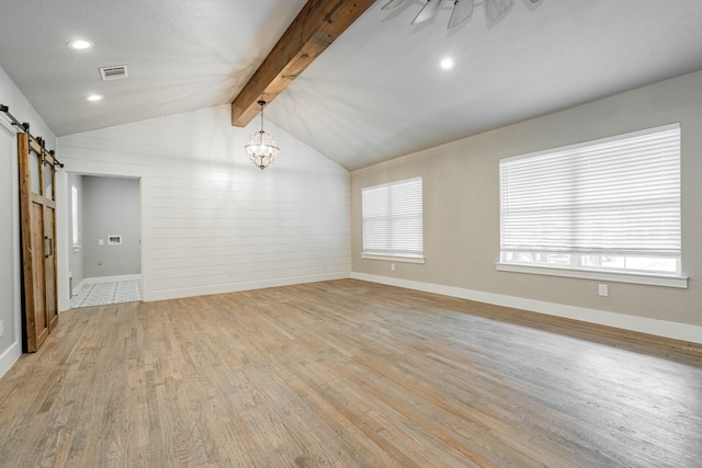 spare room with a barn door, light wood finished floors, an inviting chandelier, visible vents, and vaulted ceiling with beams