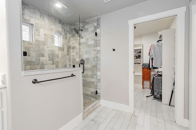 bathroom with a spacious closet, baseboards, wood finished floors, and a stall shower
