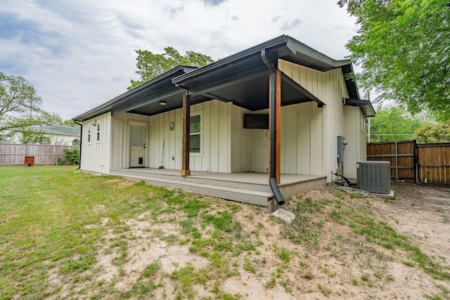 rear view of house featuring fence, board and batten siding, a yard, and central AC