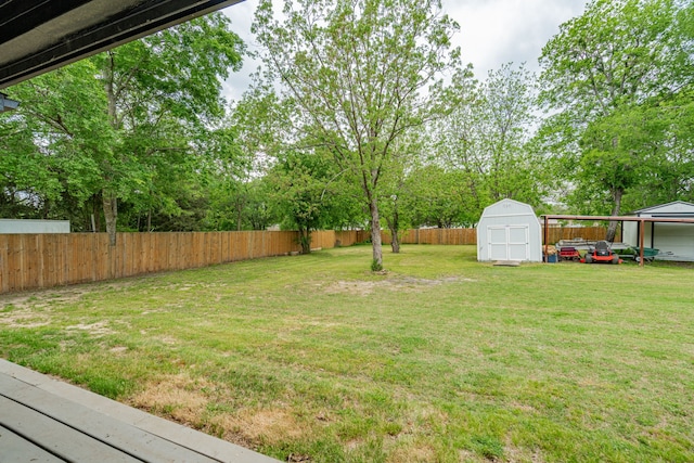view of yard with a carport, a fenced backyard, an outdoor structure, and a shed