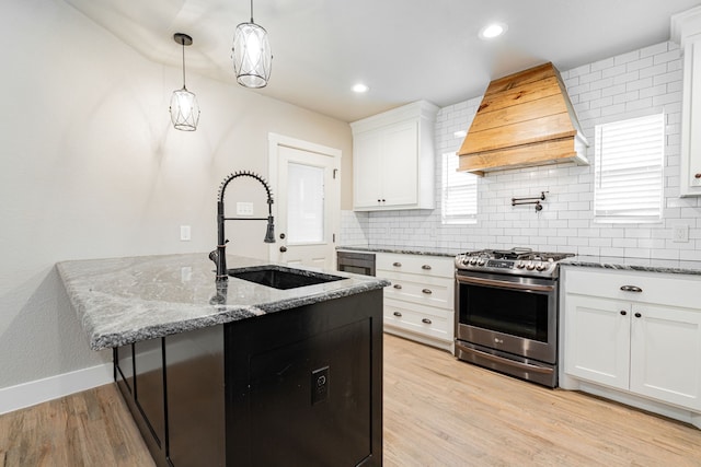 kitchen with stainless steel range with gas cooktop, a sink, custom exhaust hood, decorative backsplash, and light stone counters