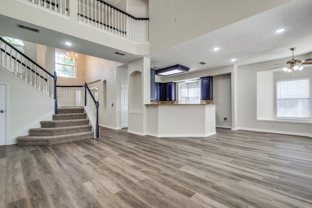 unfurnished living room featuring wood finished floors, visible vents, ceiling fan, and a high ceiling