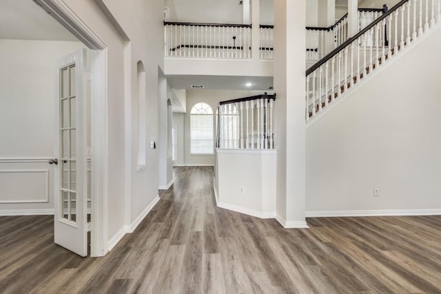 foyer entrance featuring arched walkways, wood finished floors, a towering ceiling, and baseboards