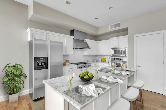 kitchen with white cabinets, visible vents, a sink, wall chimney exhaust hood, and appliances with stainless steel finishes