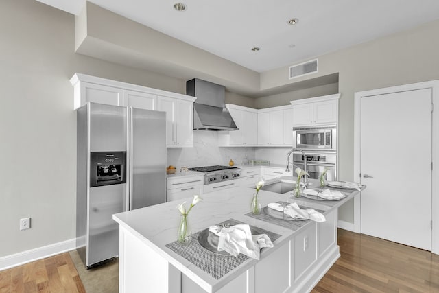 kitchen with wall chimney exhaust hood, stainless steel appliances, white cabinets, a sink, and visible vents