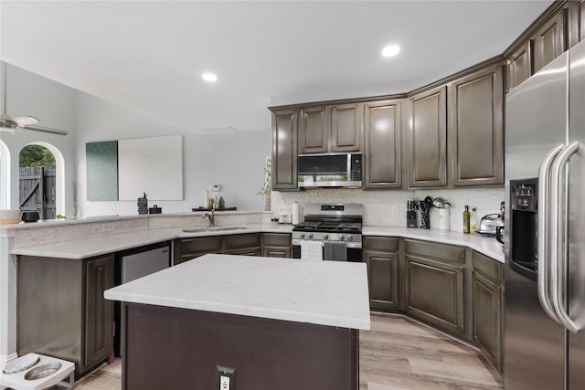 kitchen with stainless steel appliances, a peninsula, a sink, light wood-style floors, and a ceiling fan