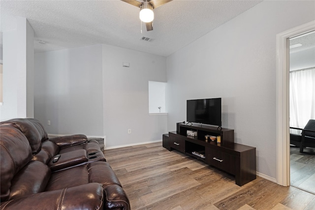 living room featuring a ceiling fan, a textured ceiling, light wood-type flooring, baseboards, and visible vents