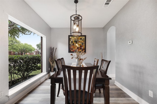 dining room with arched walkways, a wealth of natural light, wood finished floors, and visible vents