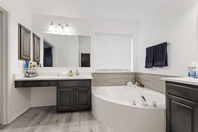 bathroom with a jetted tub, vanity, and wood finished floors