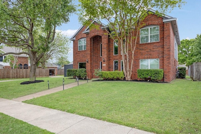traditional-style home featuring a front lawn, brick siding, and fence