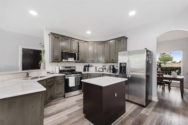 kitchen featuring light countertops, a sink, arched walkways, decorative backsplash, and appliances with stainless steel finishes