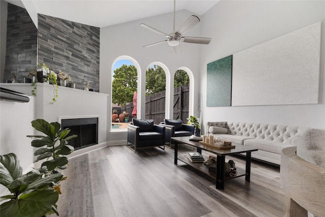 living area with high vaulted ceiling, ceiling fan, wood finished floors, and a fireplace