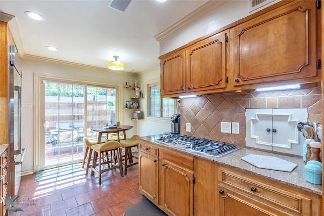 kitchen featuring brown cabinets, light stone countertops, crown molding, decorative backsplash, and appliances with stainless steel finishes