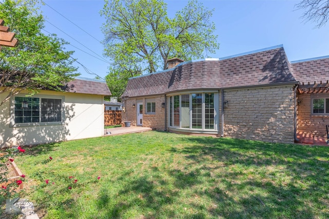 back of house featuring a lawn, a chimney, stone siding, a shingled roof, and fence