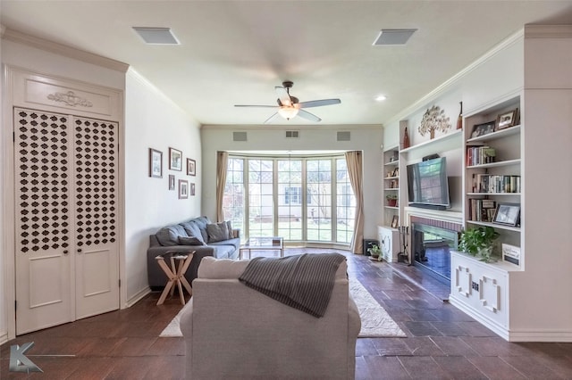 living room with visible vents, a glass covered fireplace, ceiling fan, and crown molding