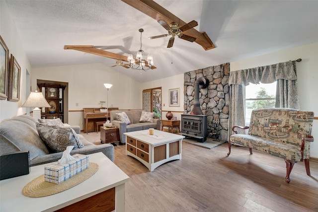 living room featuring ceiling fan with notable chandelier, lofted ceiling with beams, light wood-style floors, and a wood stove