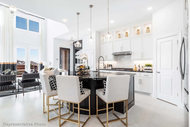 kitchen featuring cooktop, a kitchen breakfast bar, under cabinet range hood, dark countertops, and tasteful backsplash