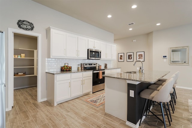 5753 Brookville Dr, Fort Worth, TX 76179 - kitchen featuring stainless steel appliances, a sink, a breakfast bar area, white cabinetry, and light stone counters