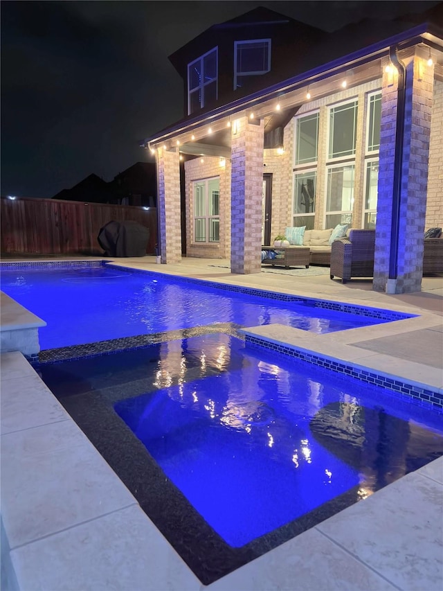 pool at night featuring fence, a pool with connected hot tub, outdoor lounge area, and a patio area