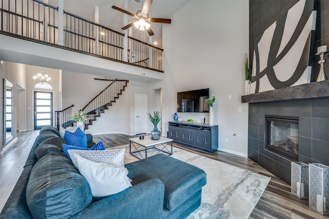 living area with a tiled fireplace, baseboards, wood finished floors, a towering ceiling, and stairway