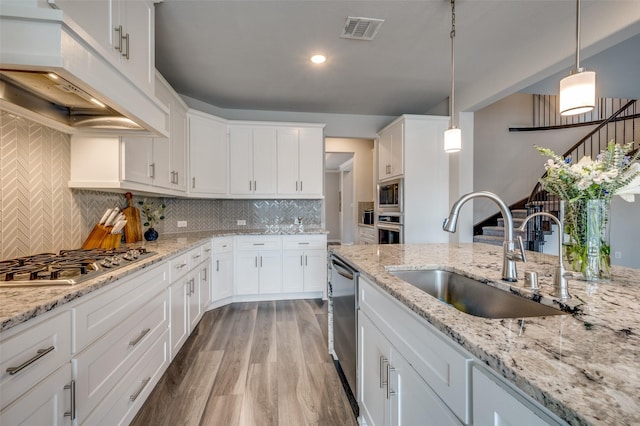 kitchen with visible vents, custom exhaust hood, white cabinetry, a sink, and stainless steel appliances