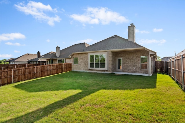 back of house featuring roof with shingles, a fenced backyard, a chimney, brick siding, and a lawn