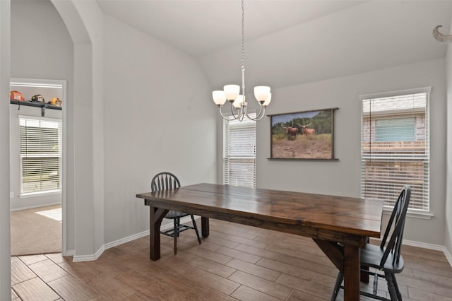 dining area featuring lofted ceiling, light wood finished floors, an inviting chandelier, arched walkways, and baseboards