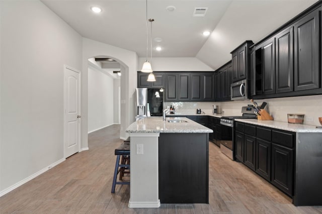 kitchen featuring stainless steel appliances, dark cabinets, visible vents, a sink, and arched walkways