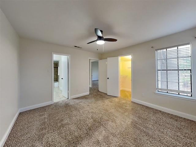 unfurnished bedroom with a spacious closet, visible vents, a ceiling fan, baseboards, and light colored carpet