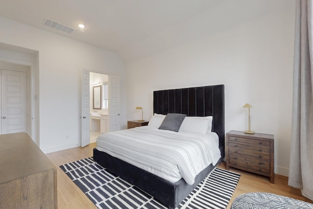 bedroom with light wood-style floors, visible vents, vaulted ceiling, baseboards, and ensuite bathroom