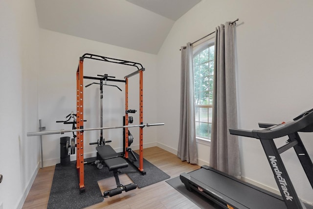 exercise area featuring vaulted ceiling, light wood-style flooring, and baseboards