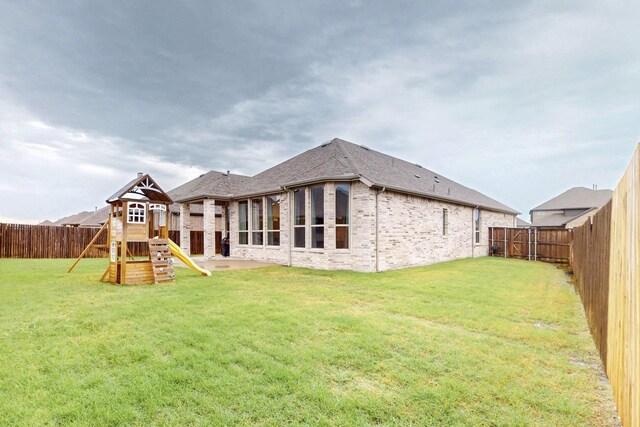 back of property with brick siding, a fenced backyard, a playground, and a lawn