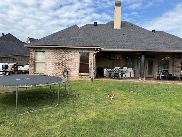 back of house with roof with shingles, a trampoline, a yard, and brick siding