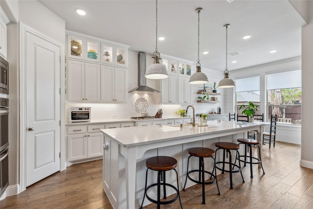 kitchen with a kitchen bar, white cabinetry, decorative backsplash, wall chimney range hood, and light countertops