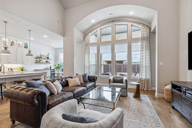 living room featuring a high ceiling, visible vents, arched walkways, and light wood-style floors