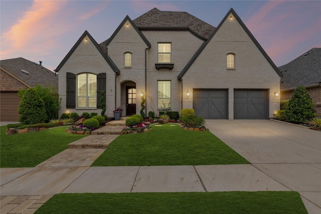 french provincial home with concrete driveway, brick siding, a garage, and a front yard