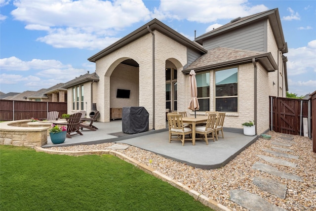 back of house featuring a gate, a fenced backyard, a patio area, a lawn, and brick siding