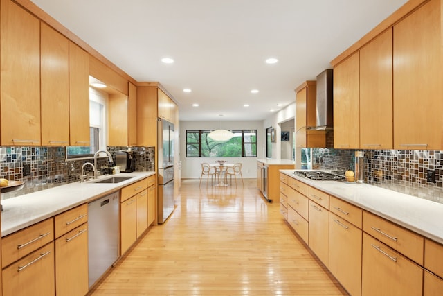 kitchen with wall chimney range hood, a sink, stainless steel appliances, light wood finished floors, and backsplash