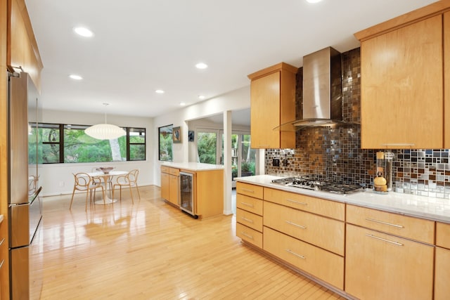 kitchen with beverage cooler, wall chimney range hood, decorative backsplash, light wood-style flooring, and appliances with stainless steel finishes