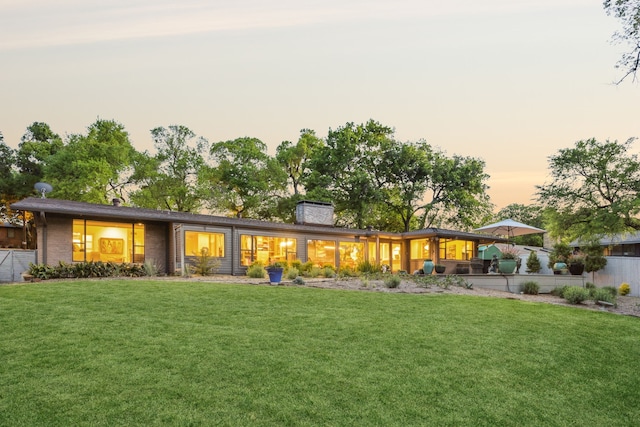 back of property at dusk with a chimney and a yard