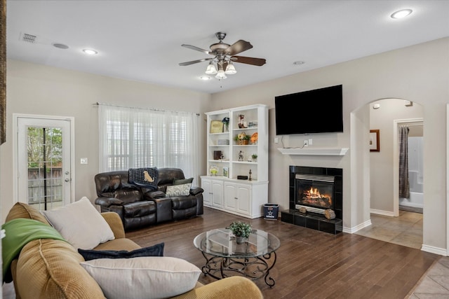living area featuring a ceiling fan, wood finished floors, arched walkways, a fireplace, and visible vents