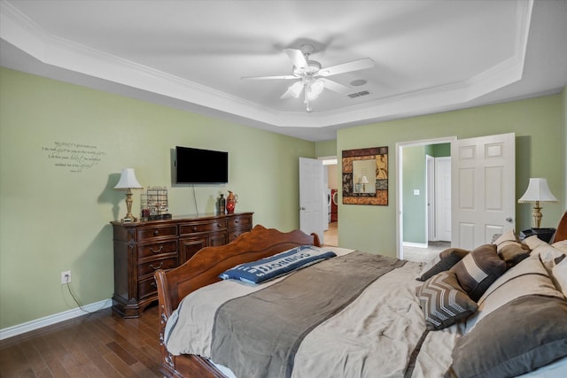 bedroom featuring a tray ceiling, wood finished floors, visible vents, ornamental molding, and baseboards