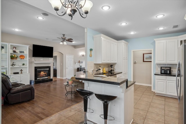 kitchen featuring a kitchen breakfast bar, freestanding refrigerator, a peninsula, open floor plan, and white cabinetry