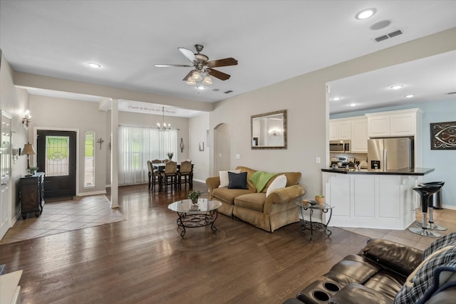living area with arched walkways, wood finished floors, visible vents, and ceiling fan with notable chandelier